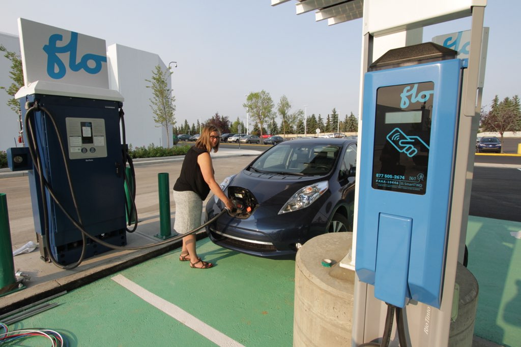 A woman charges her vehicle at a Flo charging station, demonstrating someone using EV charging station